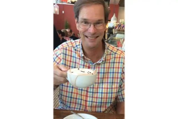 Joseph L. Rubey Jr. smiles while holding a large mug of hot chocolate at a restaurant table.