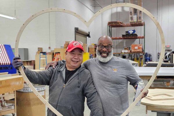Two exhibit shop team members pose with a heart-shaped structure in a fabrication workspace.