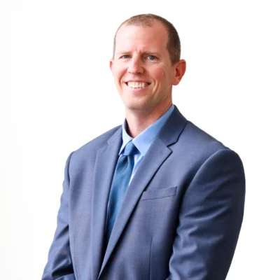 Cody Disbennet smiles in a blue suit and tie against a white background.