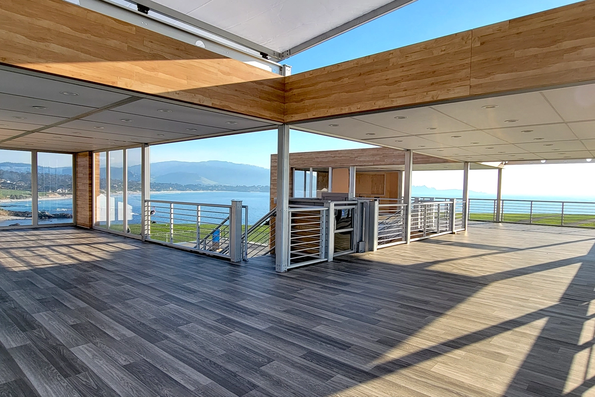Open-air upper level of an event structure with wood-look flooring, railings, and coastal views
