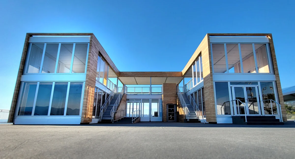 Two-story outdoor event structure with glass-walled rooms, twin staircases, and a covered upper-level deck