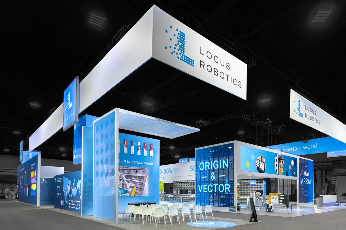 Wide view of the Locus Robotics exhibit with hanging signs, blue displays, and a warehouse demonstration area.
