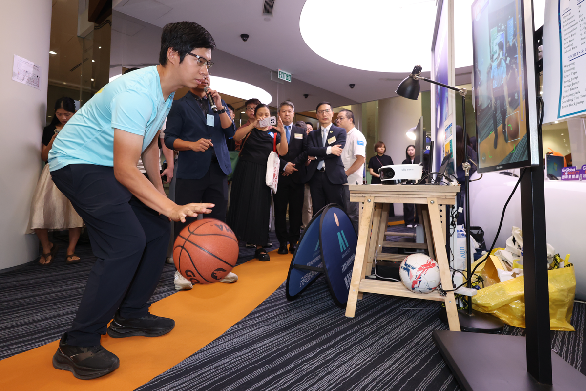A participant dribbles a basketball in front of Manna Pacific’s fitness screen as attendees watch.