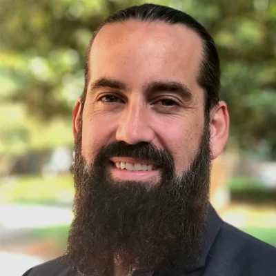 Nathan Reiser smiles in an outdoor headshot with trees in the background.