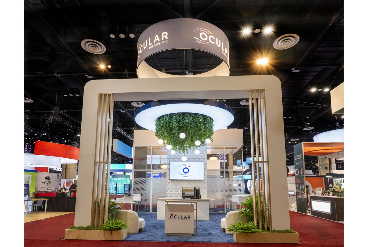 Ocular Therapeutix exhibit with a large cream-colored arch, circular hanging sign, illuminated canopy, greenery, and seating