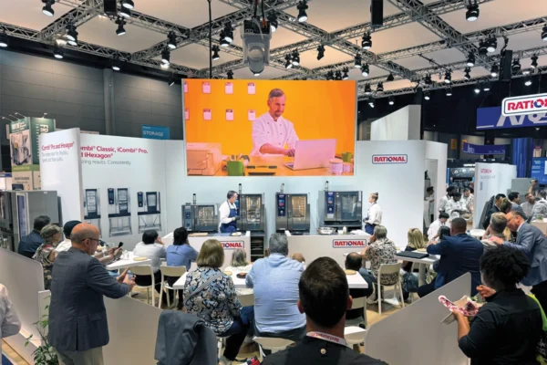 Attendees watch a RATIONAL USA cooking demonstration beneath a large LED screen