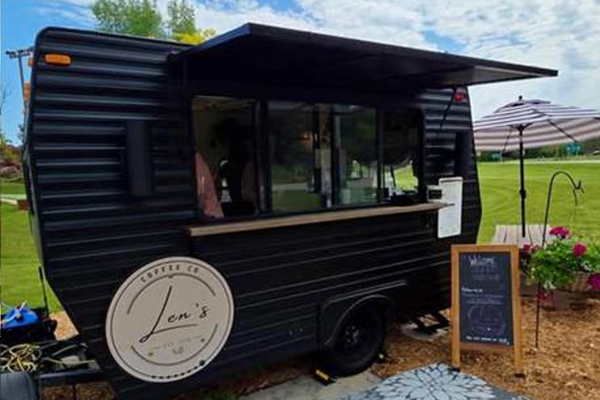Black mobile coffee trailer with an open service window parked on a lawn