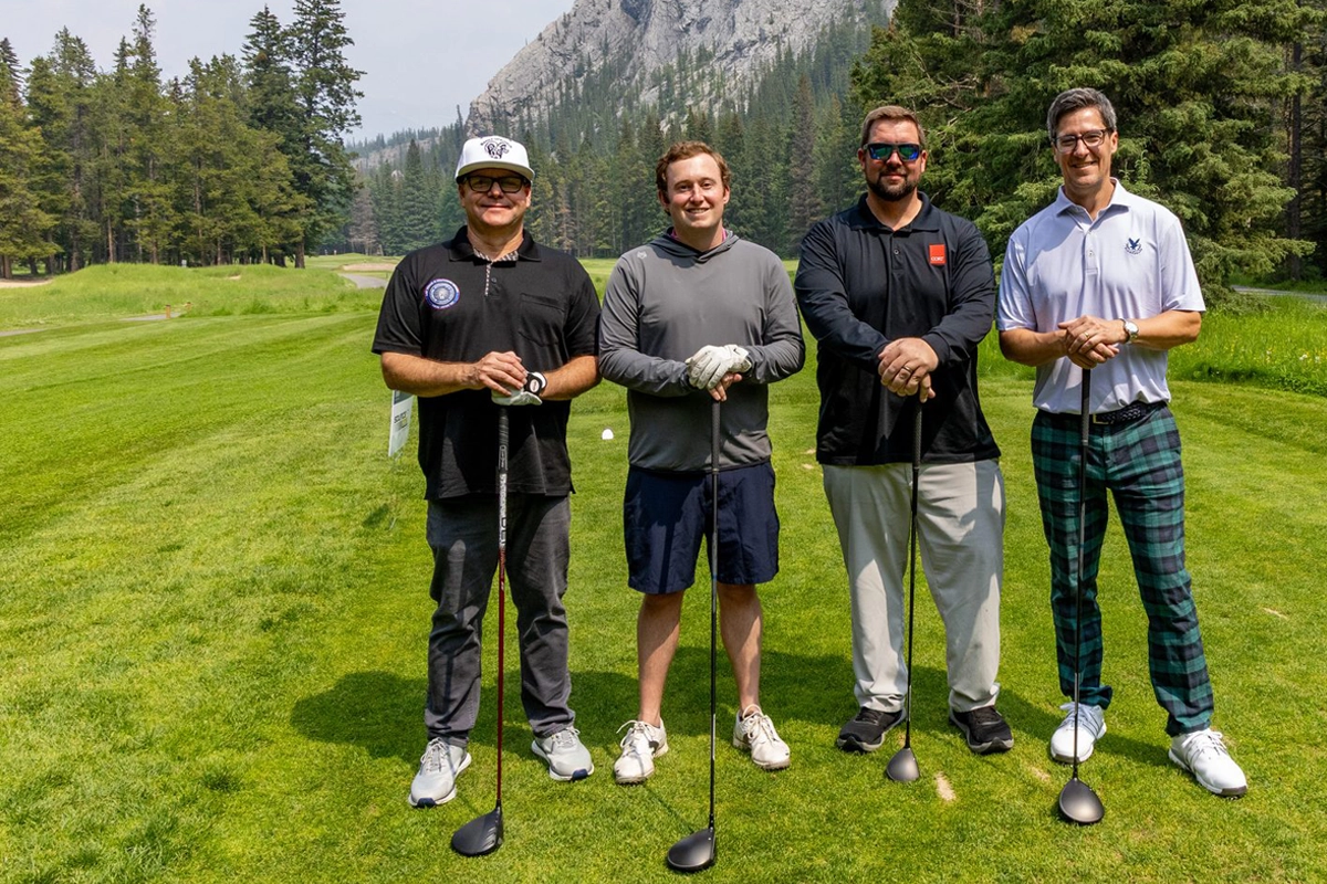 Four golfers posing on a course surrounded by trees and mountains in Banff