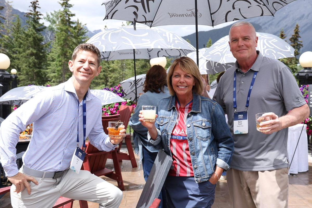 Three attendees holding drinks at an outdoor ESCA conference gathering in Banff