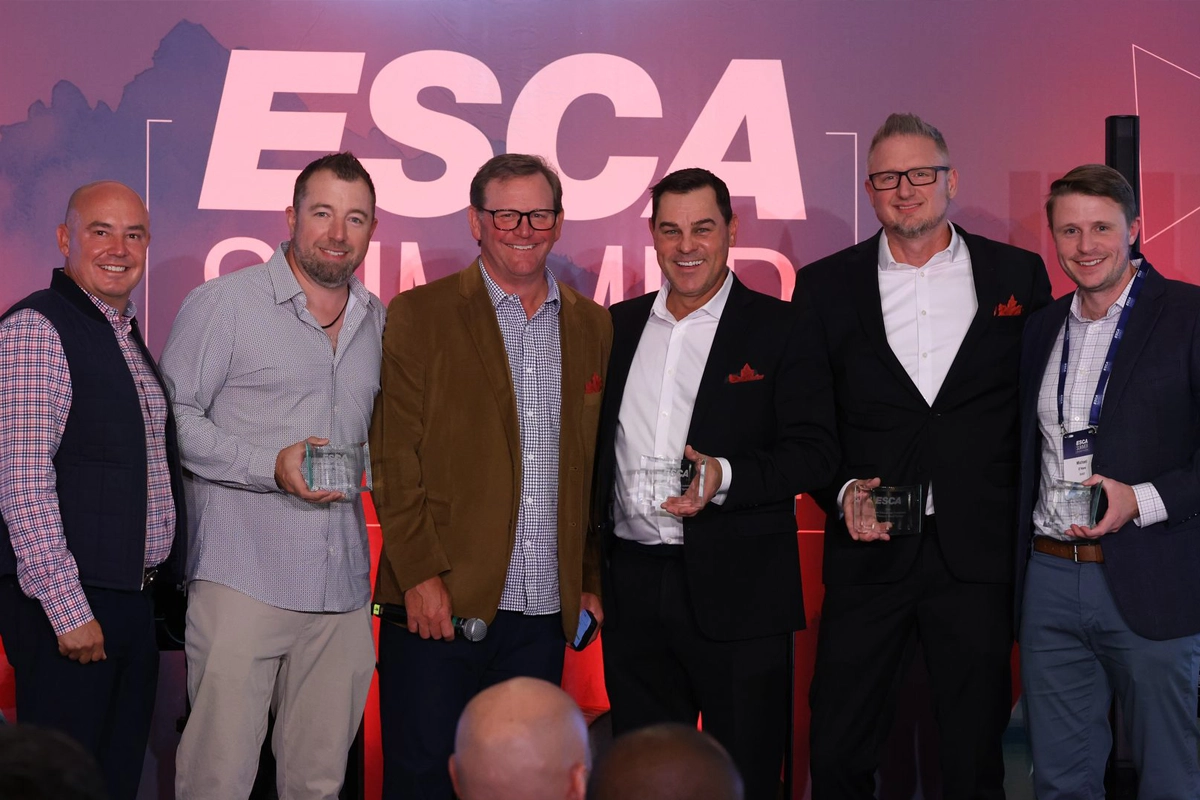 Six people posing onstage at an ESCA event, several holding glass awards