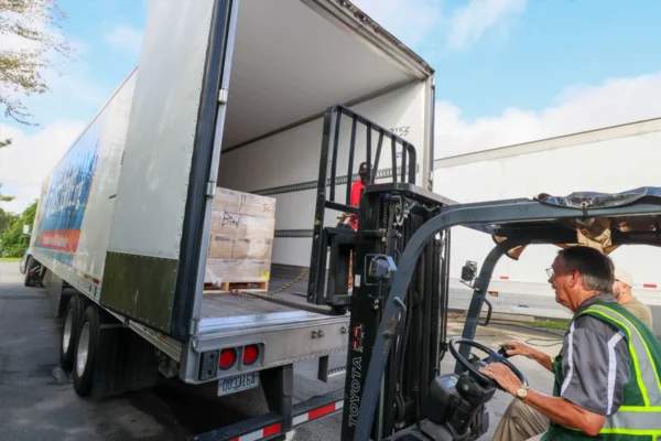 Forklift operator loading a pallet into the back of a freight truck