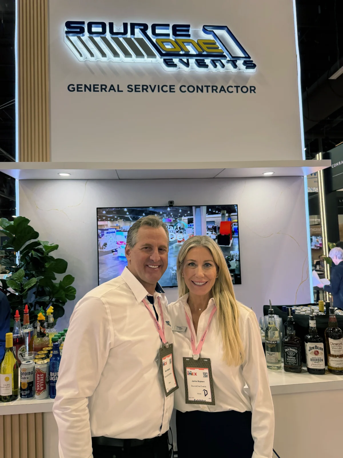 Mike and Jackie Bojesen stand together in white shirts beneath Source One Events signage at their exhibit.