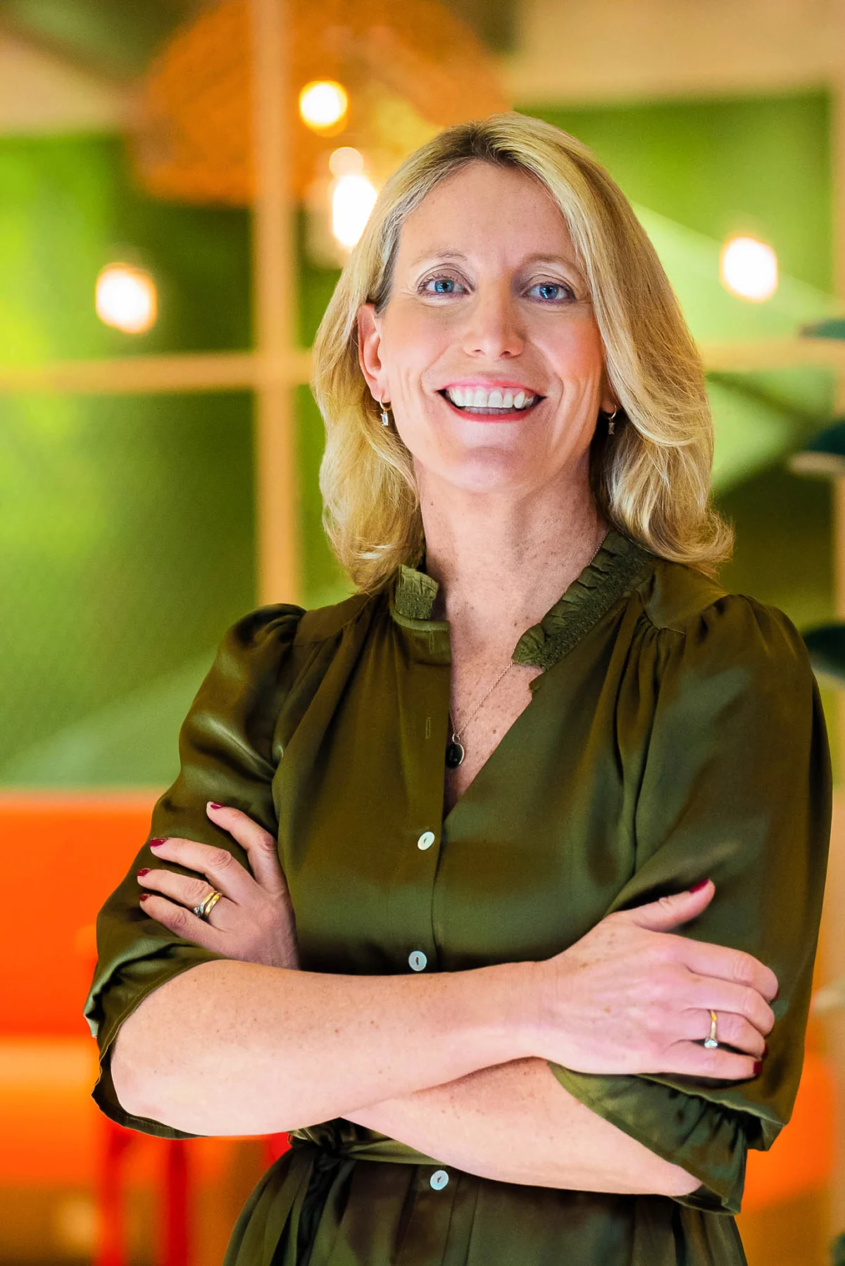 Lisa Hannant smiles with her arms crossed, wearing an olive-green dress.
