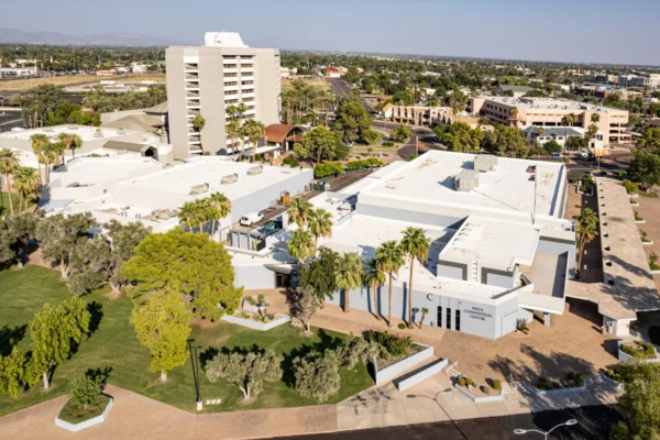 Aerial view of Mesa Convention Center in Mesa, Arizona, surrounded by palm trees, landscaped grounds, and nearby buildings.
