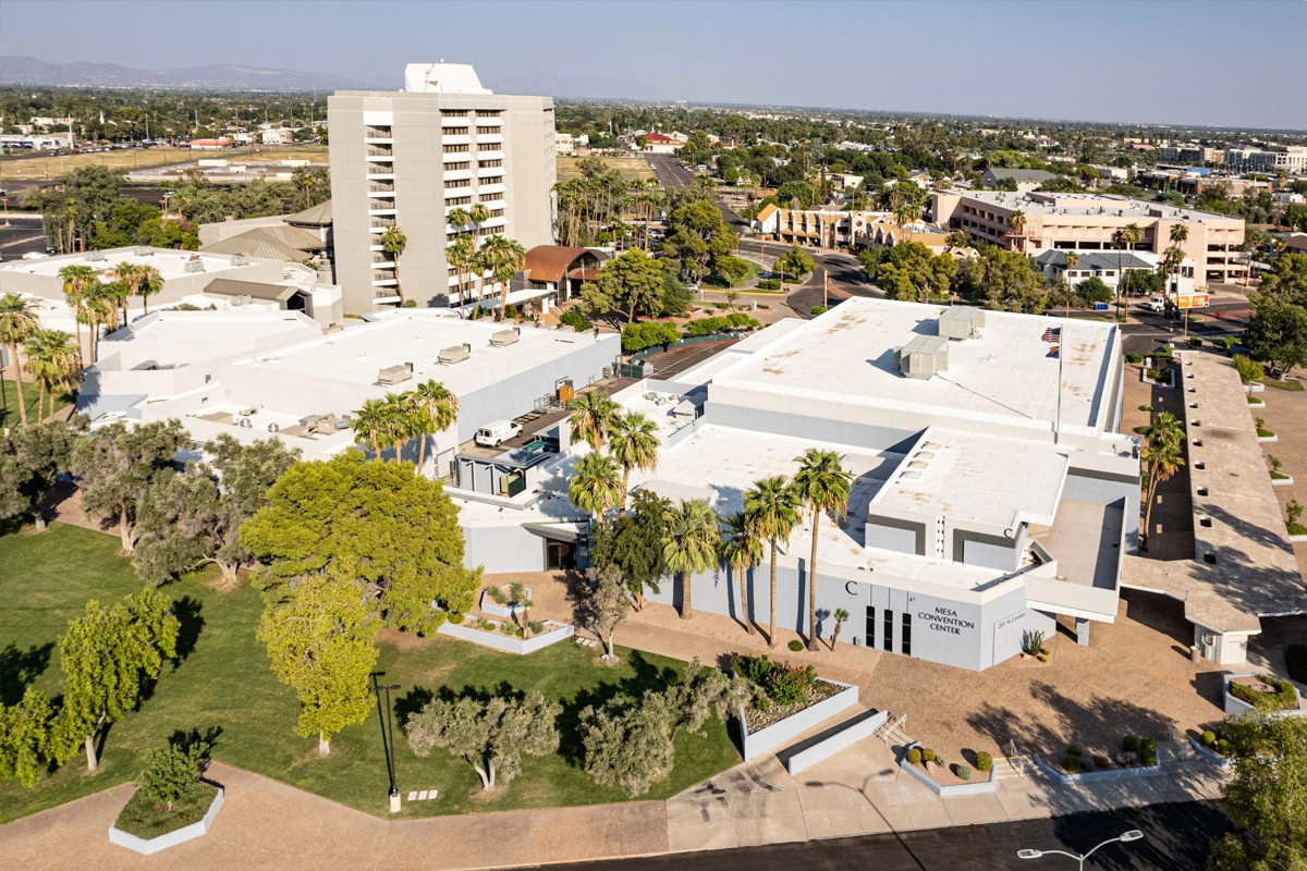 Aerial view of Mesa Convention Center in Mesa, Arizona, surrounded by palm trees, landscaped grounds, and nearby buildings.