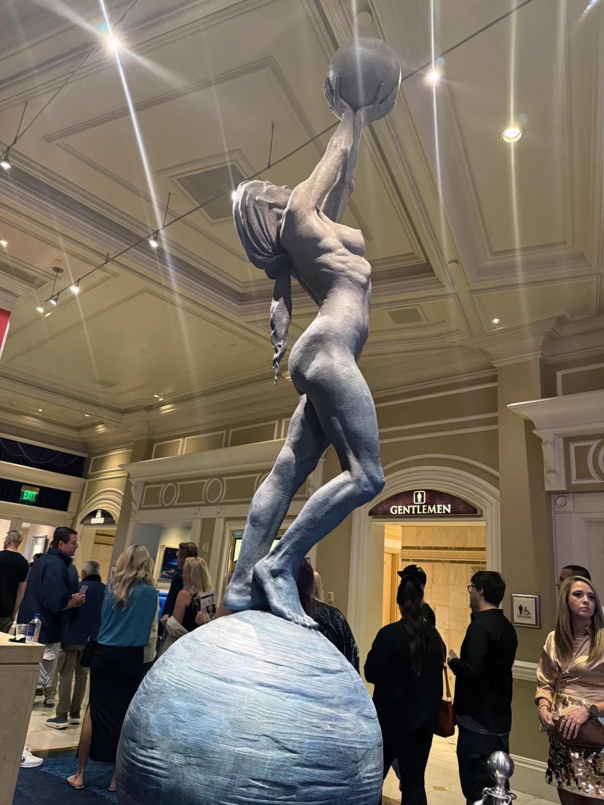 A sculpture of a figure holding a sphere overhead rises above guests in Bellagio’s “O” theater lobby.