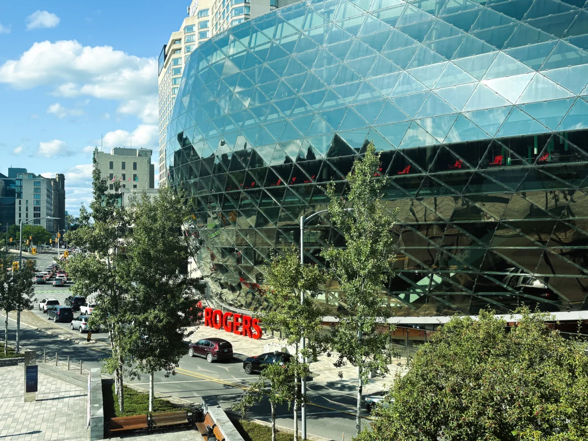 Rogers Centre Ottawa’s curved glass exterior with red Rogers signage, trees and street traffic.