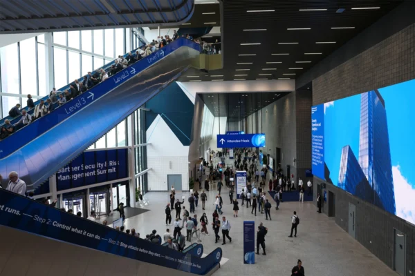 Attendees at Excel London U.S. events and international conferences move through a spacious concourse with escalators, exhibition signage, and digital displays.