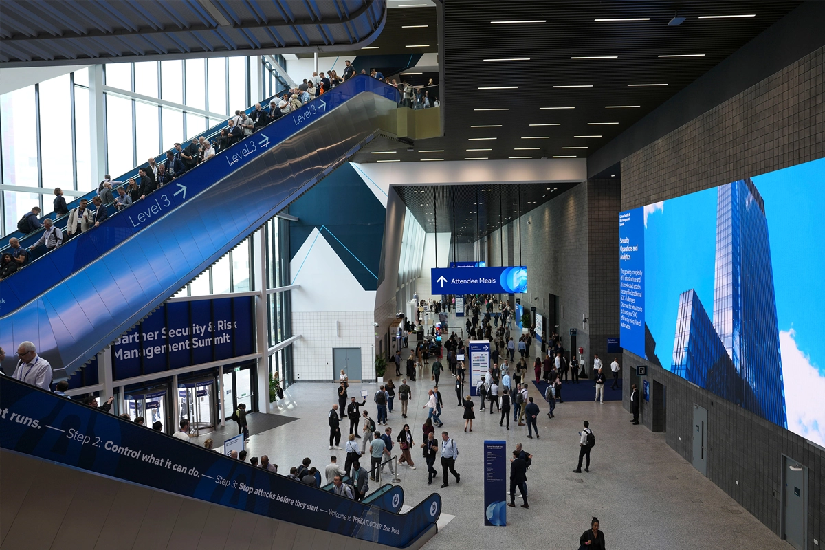 Attendees at Excel London U.S. events and international conferences move through a spacious concourse with escalators, exhibition signage, and digital displays.