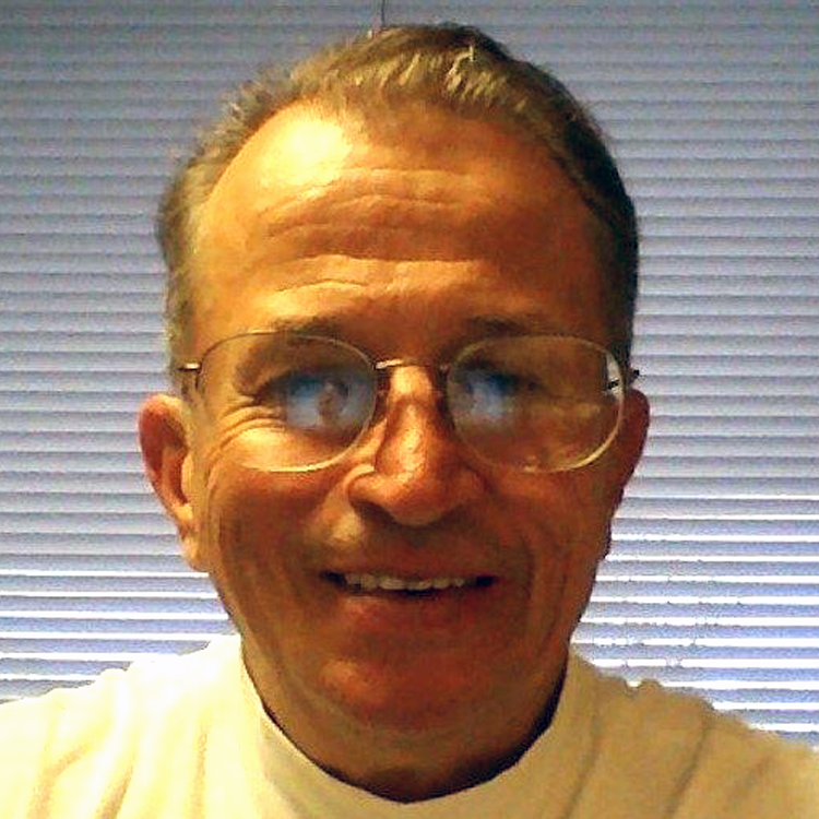 Mike Drobick smiles while wearing glasses and a white shirt in front of window blinds.