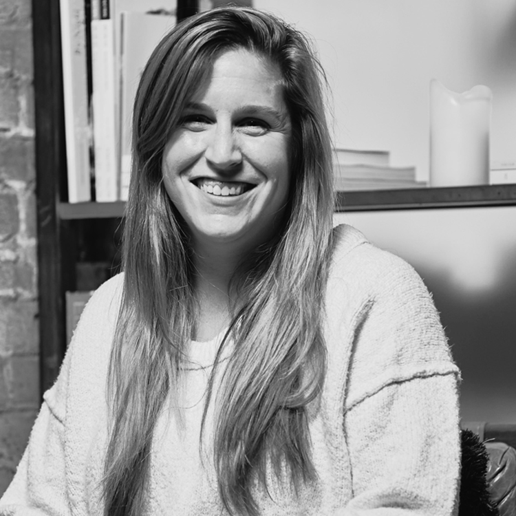 Black-and-white portrait of Erin Kana smiling in front of shelving.