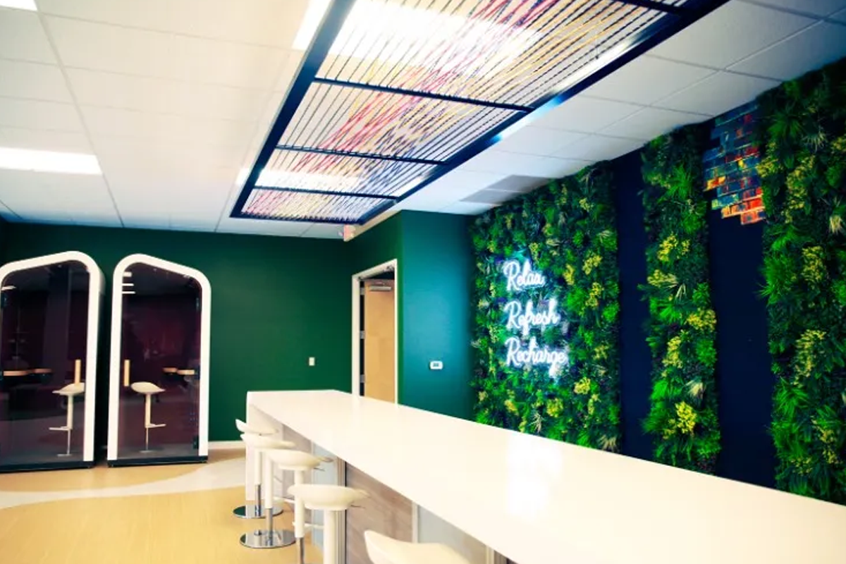 Orbus engagement area with a long white table, stools, enclosed seating pods and greenery beneath a “Relax Refresh Recharge” sign.