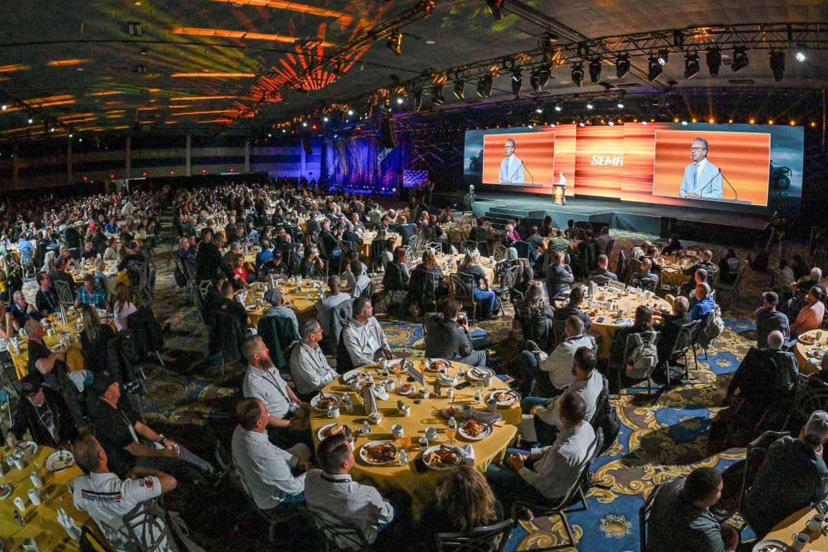 Attendees sit at round breakfast tables facing a stage with large screens and SEMA branding.